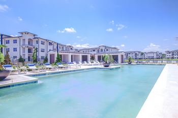 a large pool with lounge chairs and buildings in the background